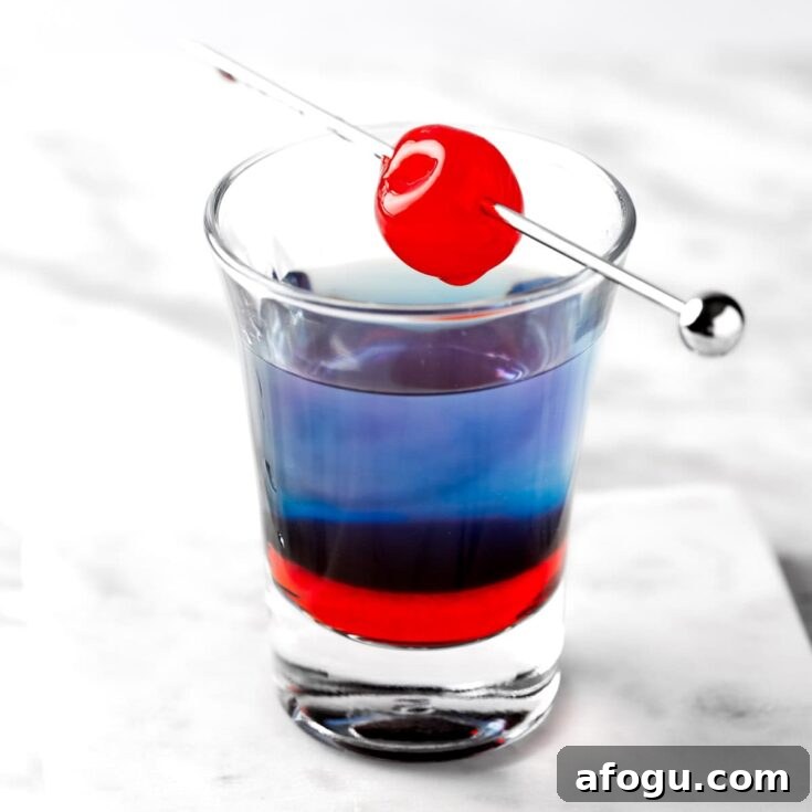 A layered Astro Pop Shot garnished with a cherry.