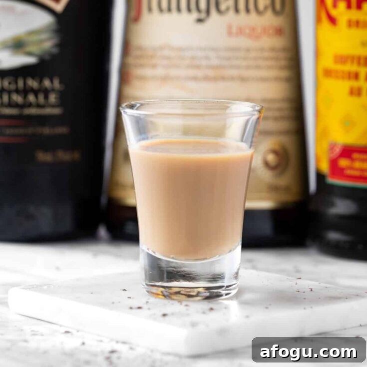 A Snickers Shot with bottles of Baileys, Frangelico and Kahlua in the background.
