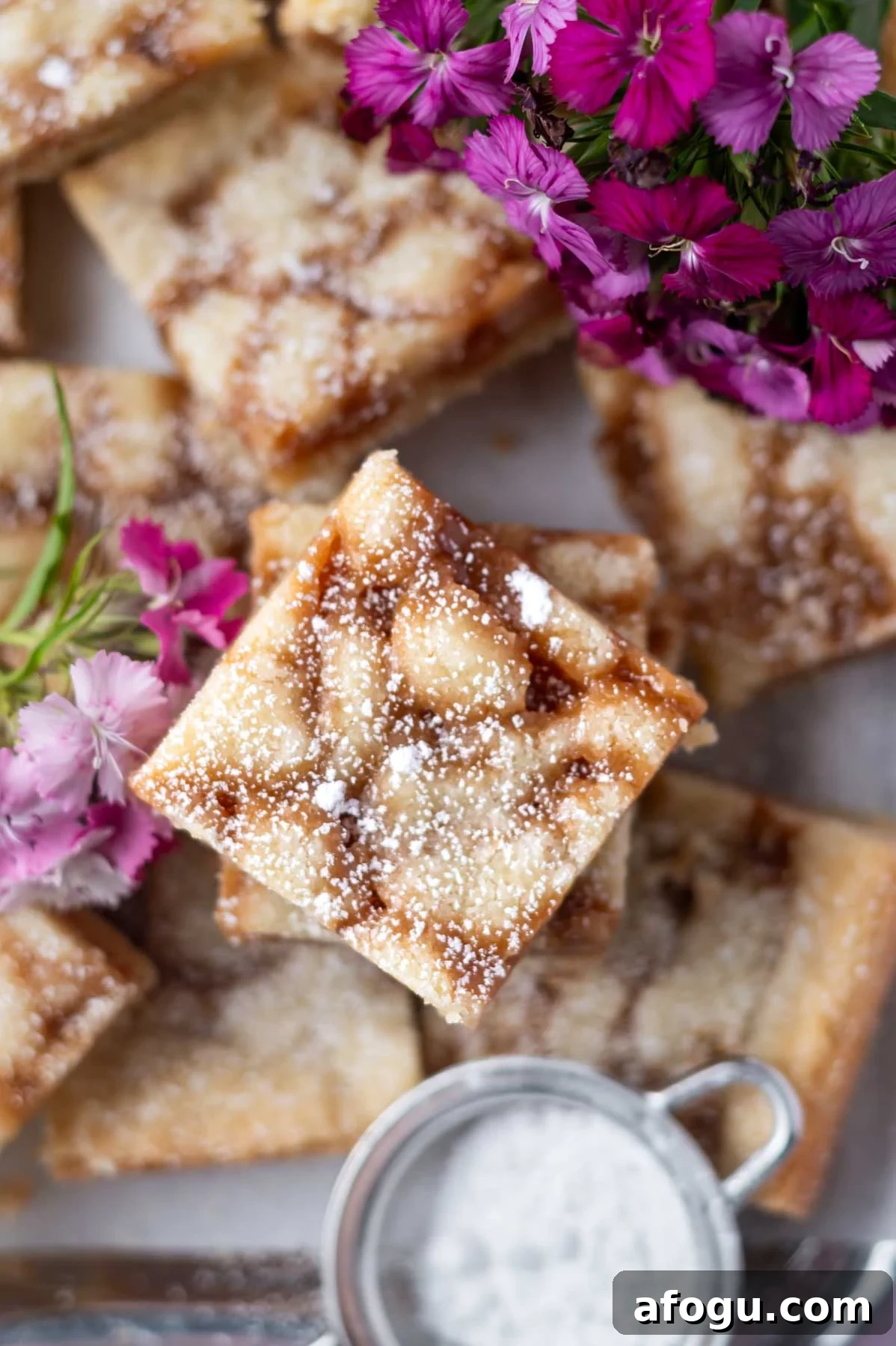 overhead look at caramel cookie bars with confectioners' sugar dusted over the top and fresh pink flowers