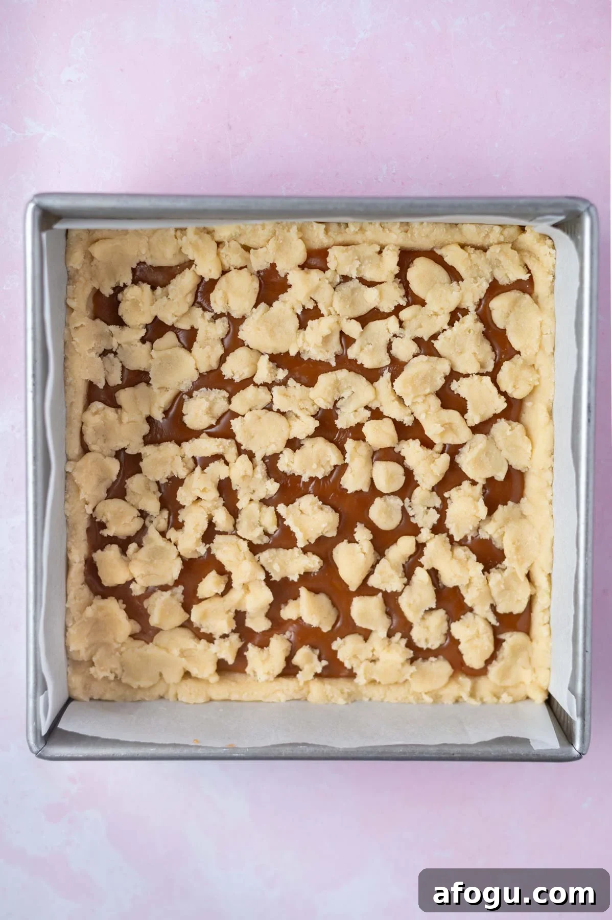 cookie dough crumbled over caramel in a baking tin