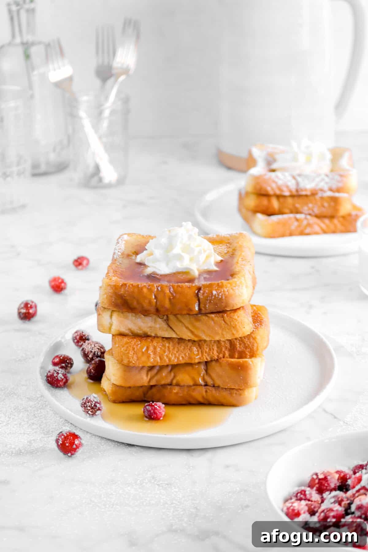 Eggnog French Toast Recipe: Festive Holiday Brunch Idea 7 french toast on a white plate with more behind, cranberries, forks, and a pitcher