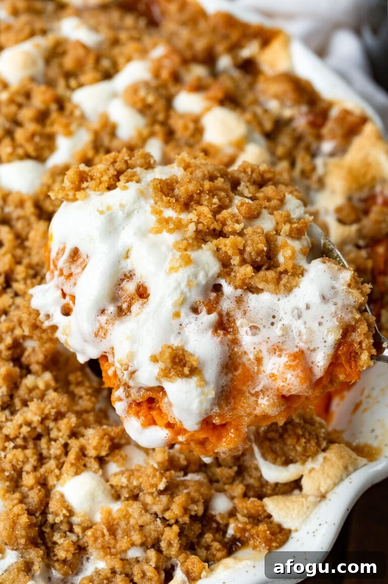 a photo of a large spoon removing a serving of sweet potato casserole topped with melted marshmallows and brown sugar streusel
