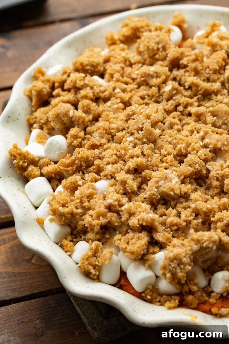 a photo of an unbaked orange vegetable casserole topped with mini marshmallows and a brown sugar streusel