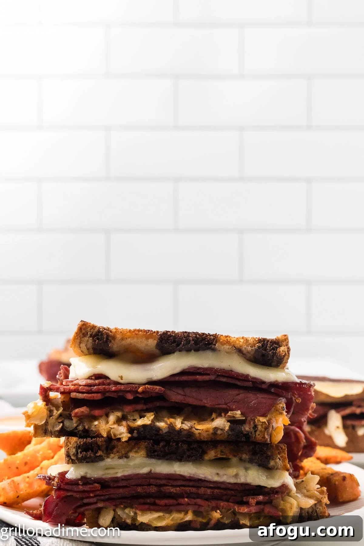 Reuben Sandwich cut in half stacked on a plate with french fries in the background