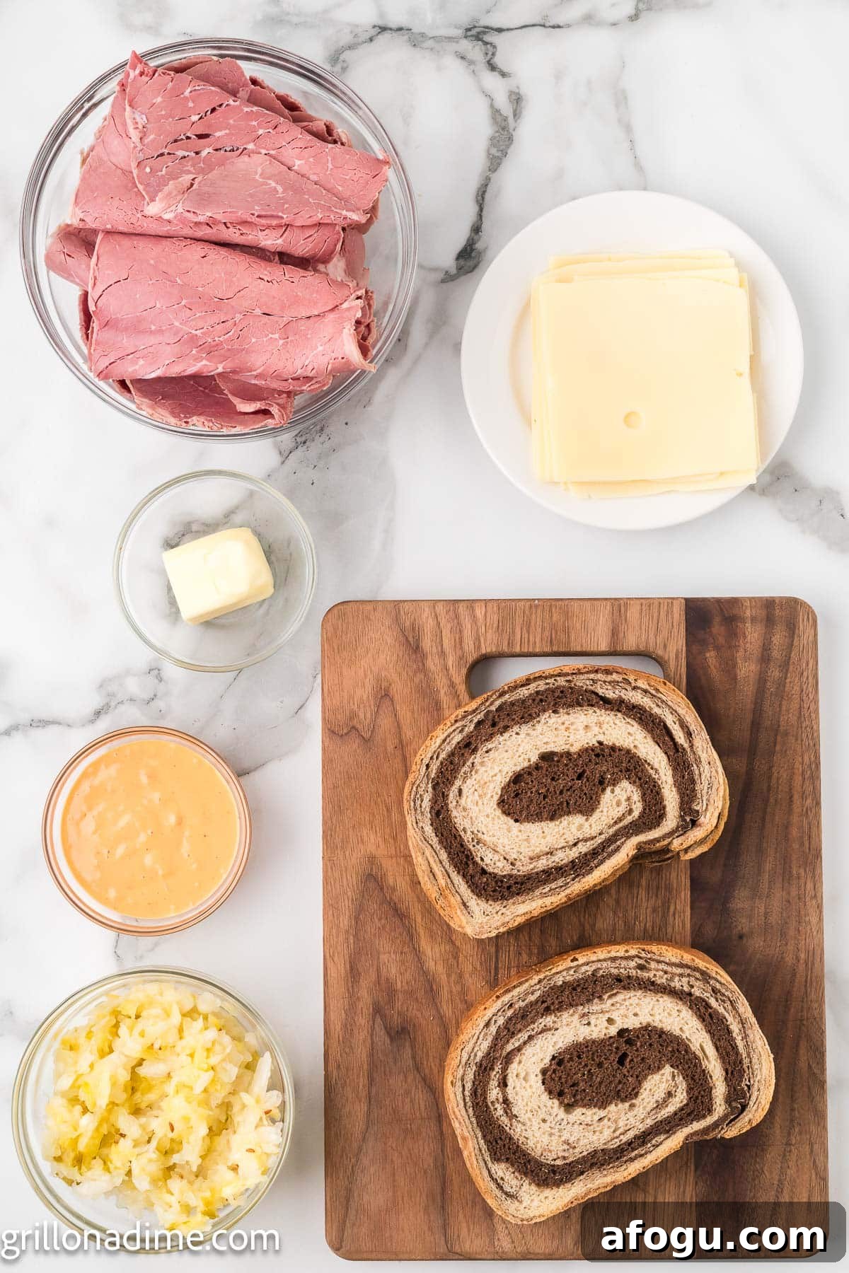 Corned beef sliced in a bowl, cheese slices on a plate, butter in a bowl, slices of rye bread on a butting board, a bowl of sauerkraut and Thousand Island Dressing