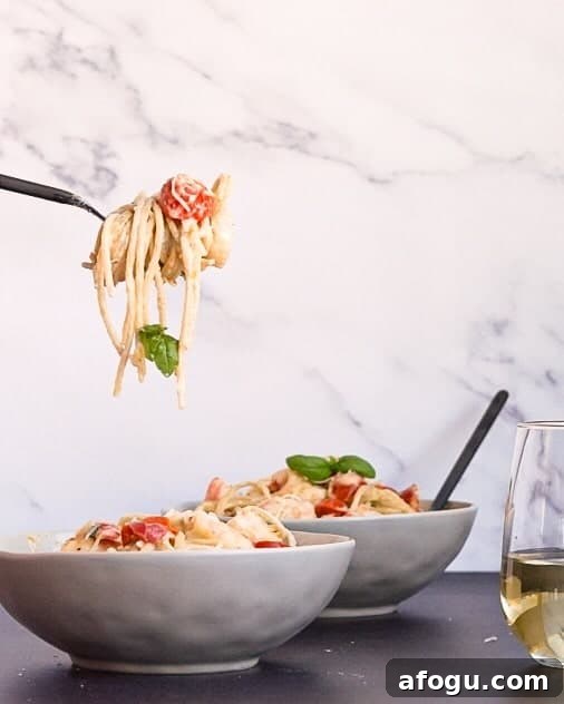 A fork twirling gluten free shrimp carbonara next to a glass of wine.