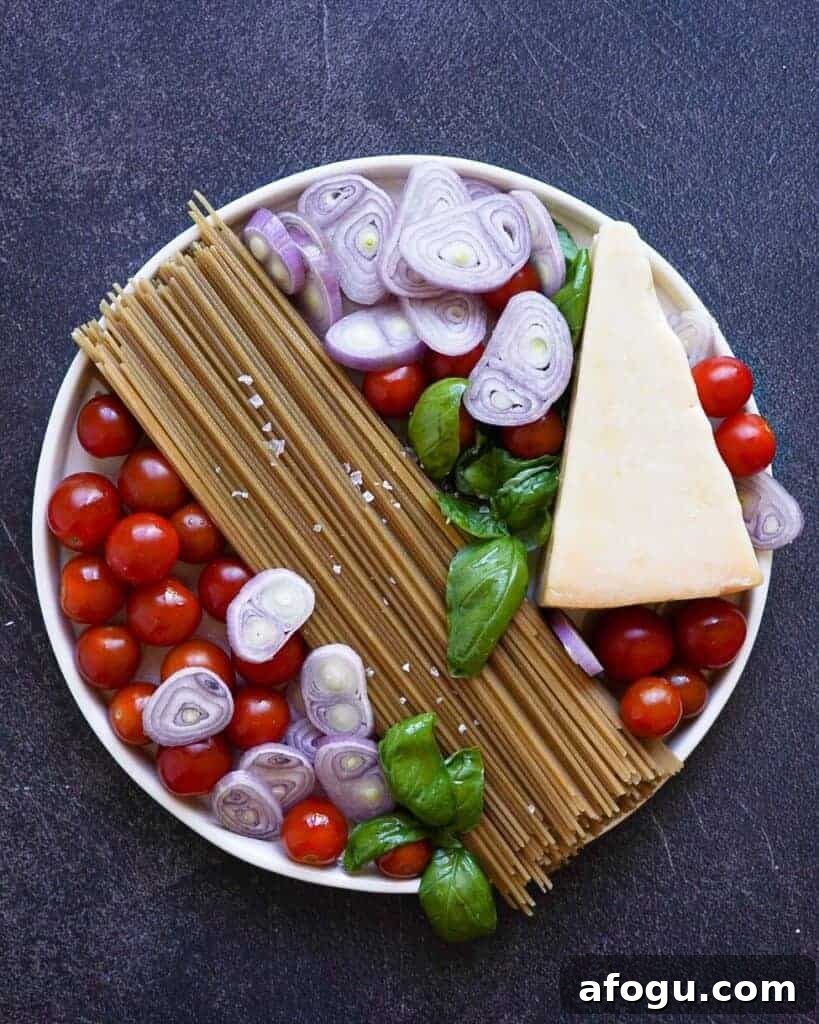 A plate with pasta, tomatoes, shallots, cheese and basil.