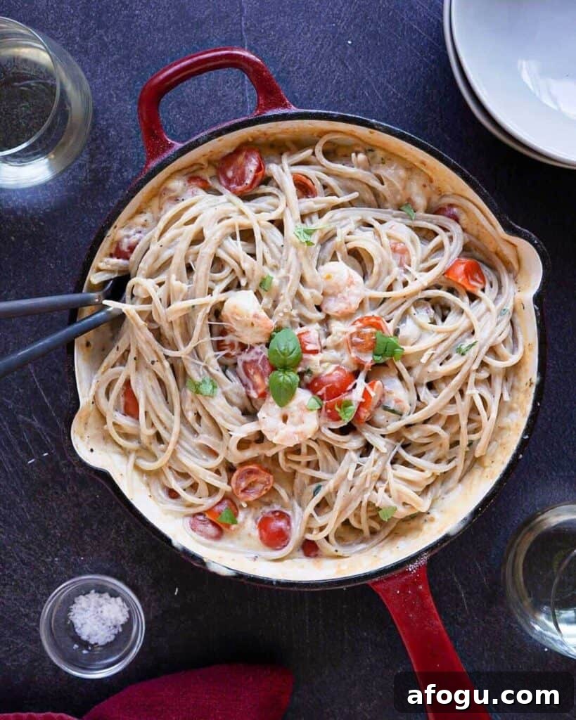 A frying pan full of shrimp carbonara with tomatoes and basil.