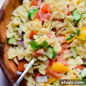 A spoon is holding some of the bowtie pasta salad with Italian dressing