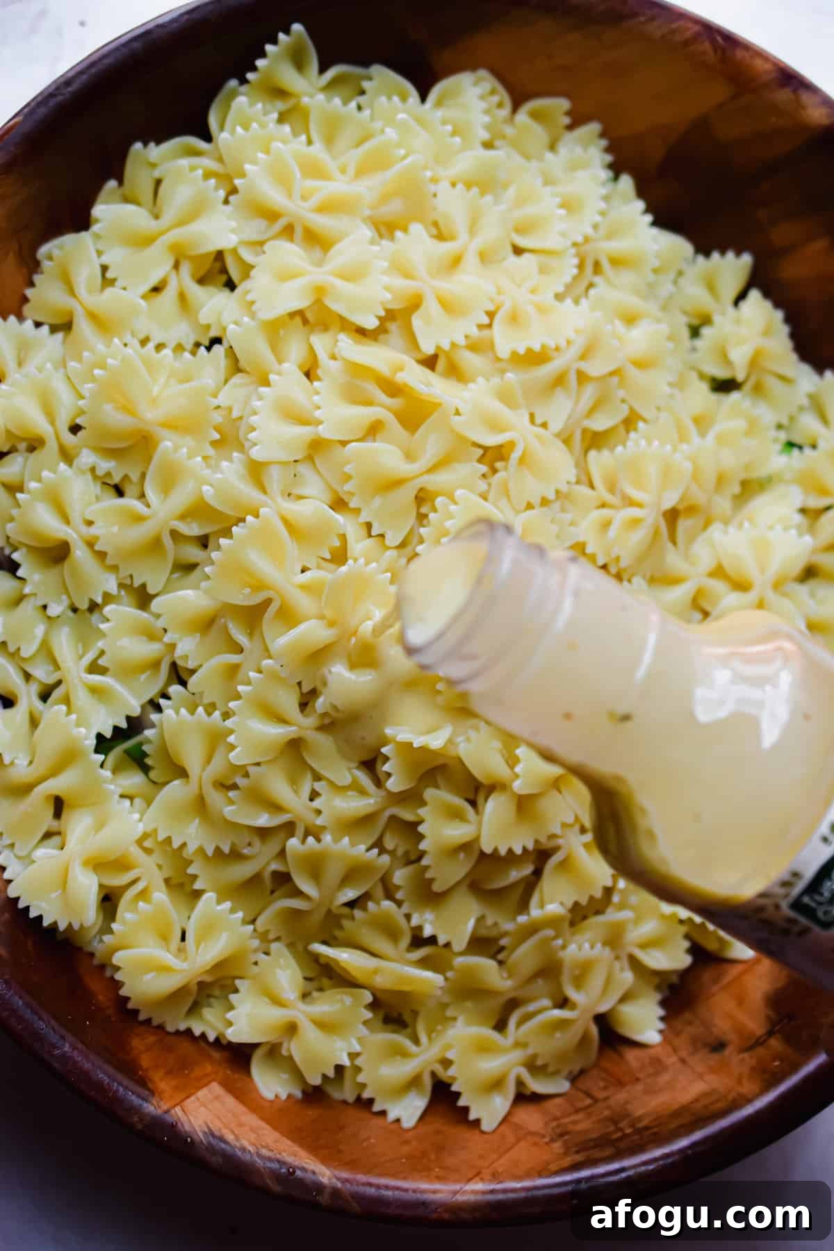 The Italian dressing is being poured into the bowl on top of the pasta.