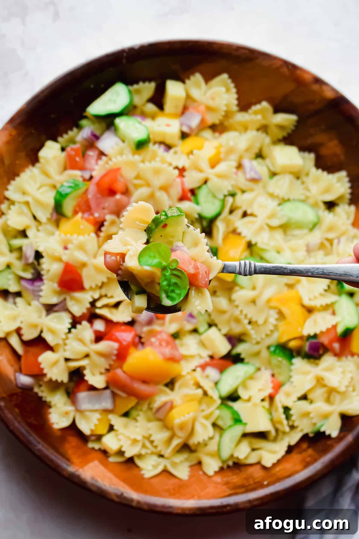 A spoon is holding  a portion of the Bowtie Pasta Salad with italian Dressing over the large bowl.
