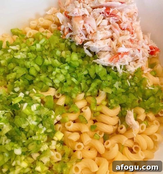 Bowl with cooked macaroni, chopped celery, onion, and crab meat.
