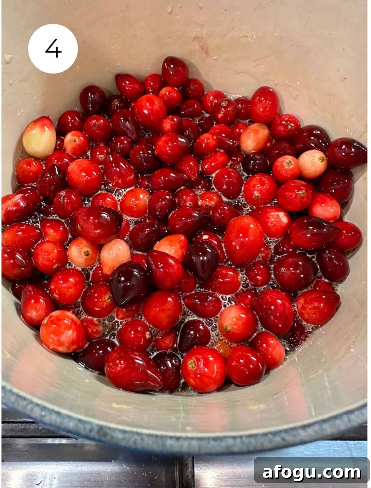 Fresh cranberries with liquid ingredients in a pan on the stove.