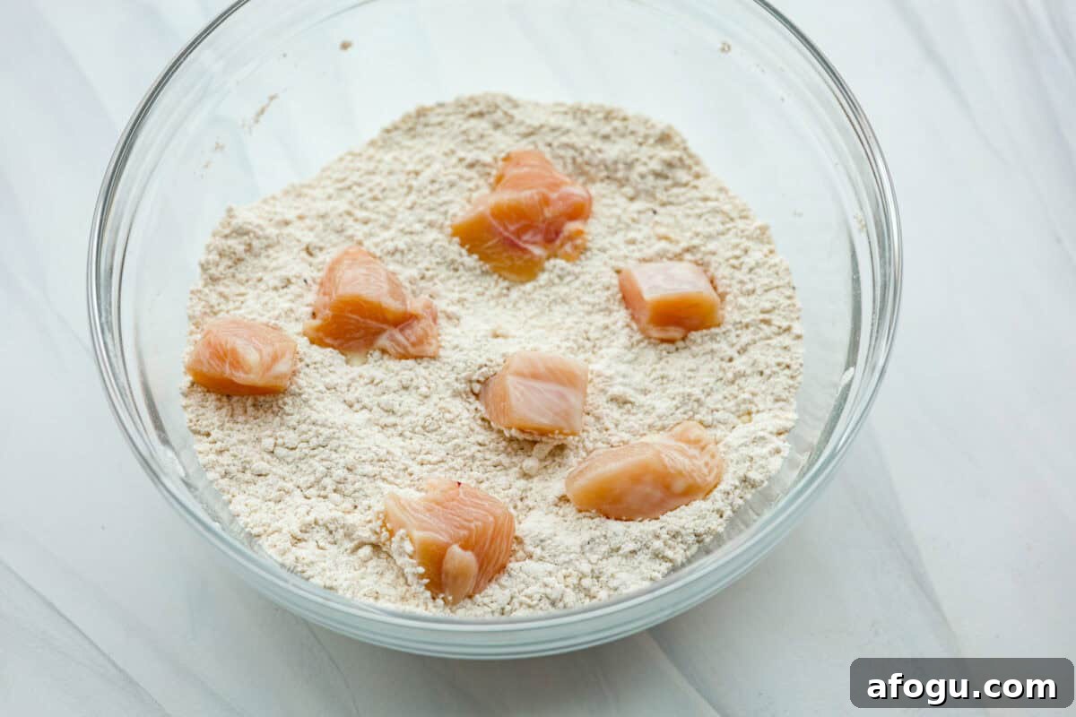 Raw chicken being coated with the dry ingredients in a glass bowl. 