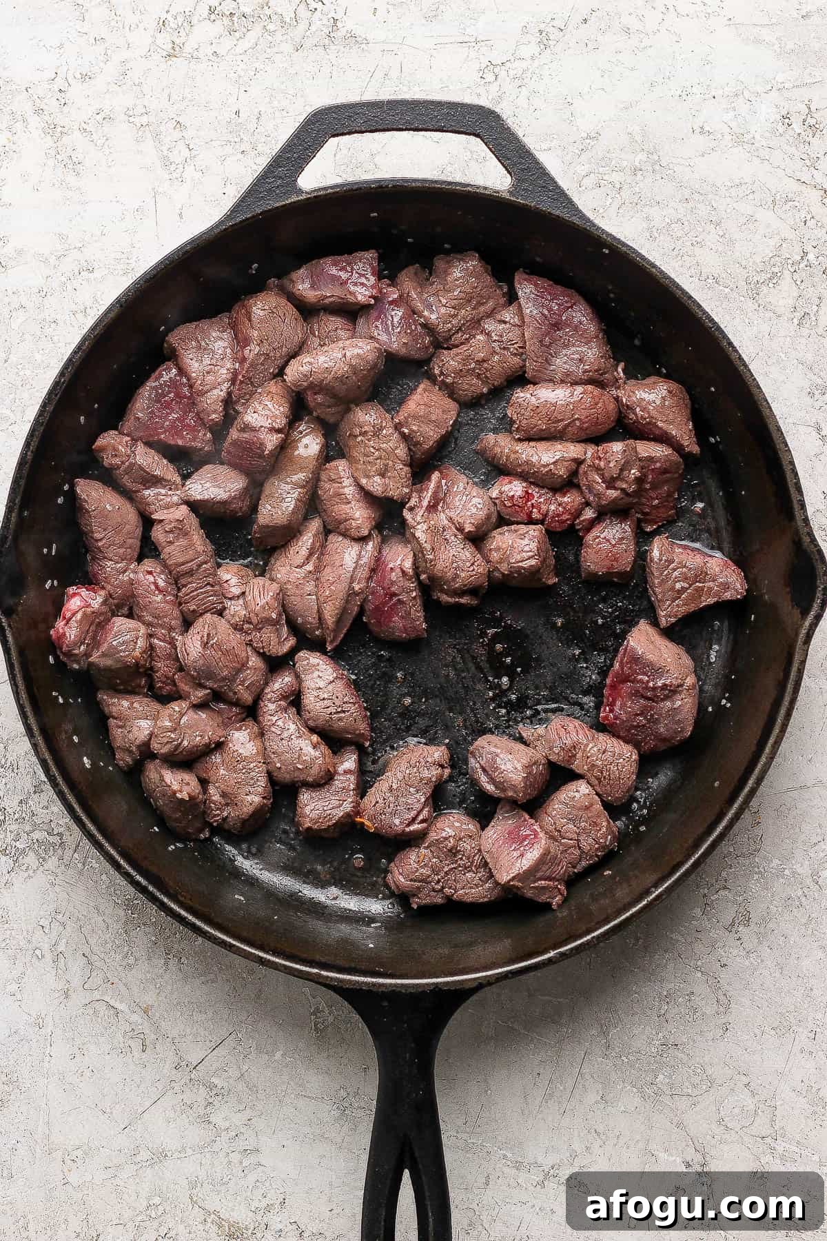 Cast iron skillet with venison searing inside.