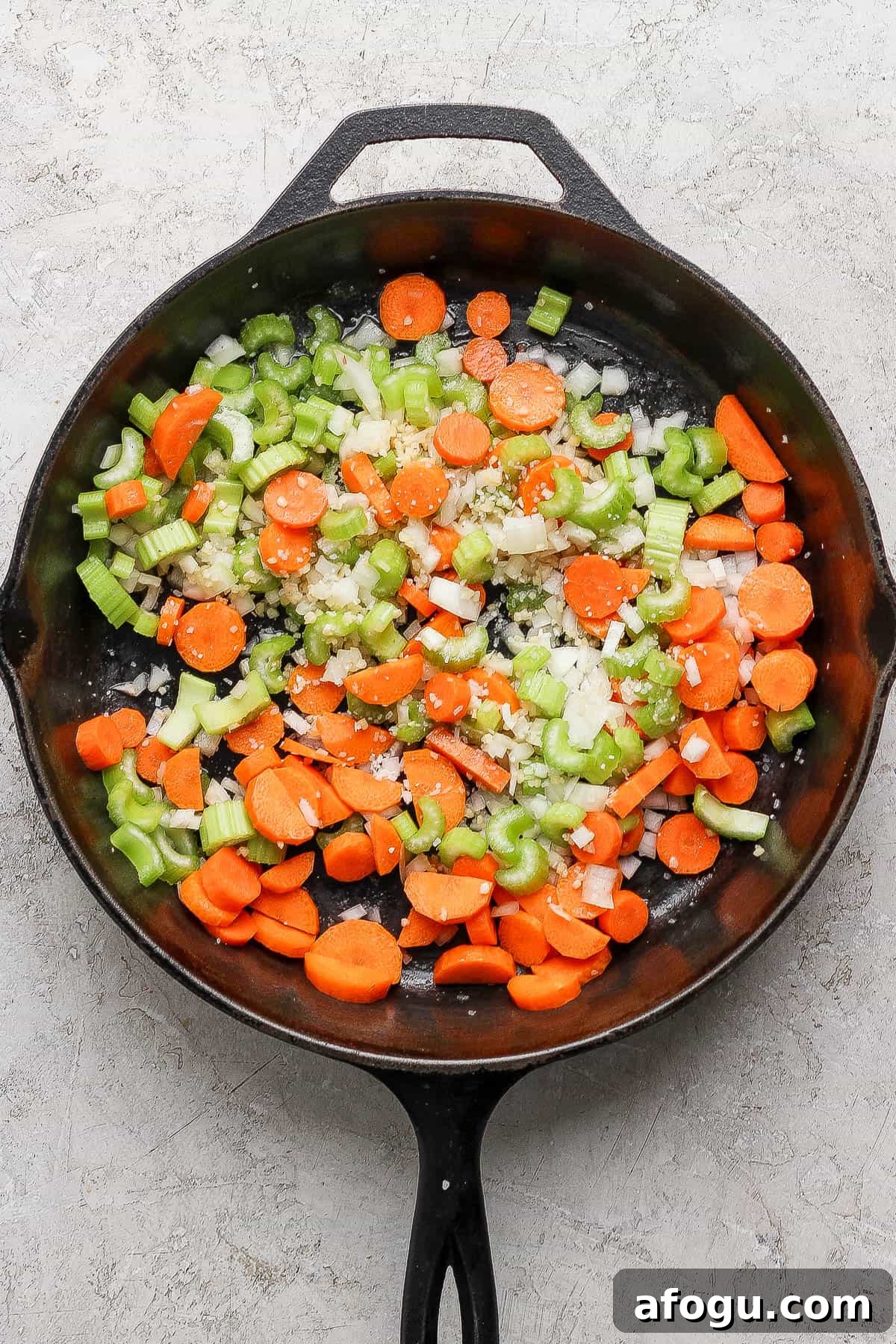 Cast iron skillet with carrot, onions and celery cooking inside.