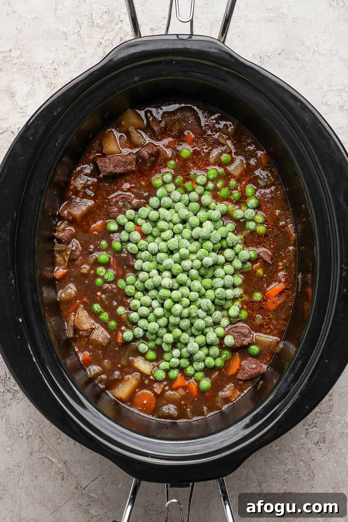 A crockpot full of venison stew with peas on top. 
