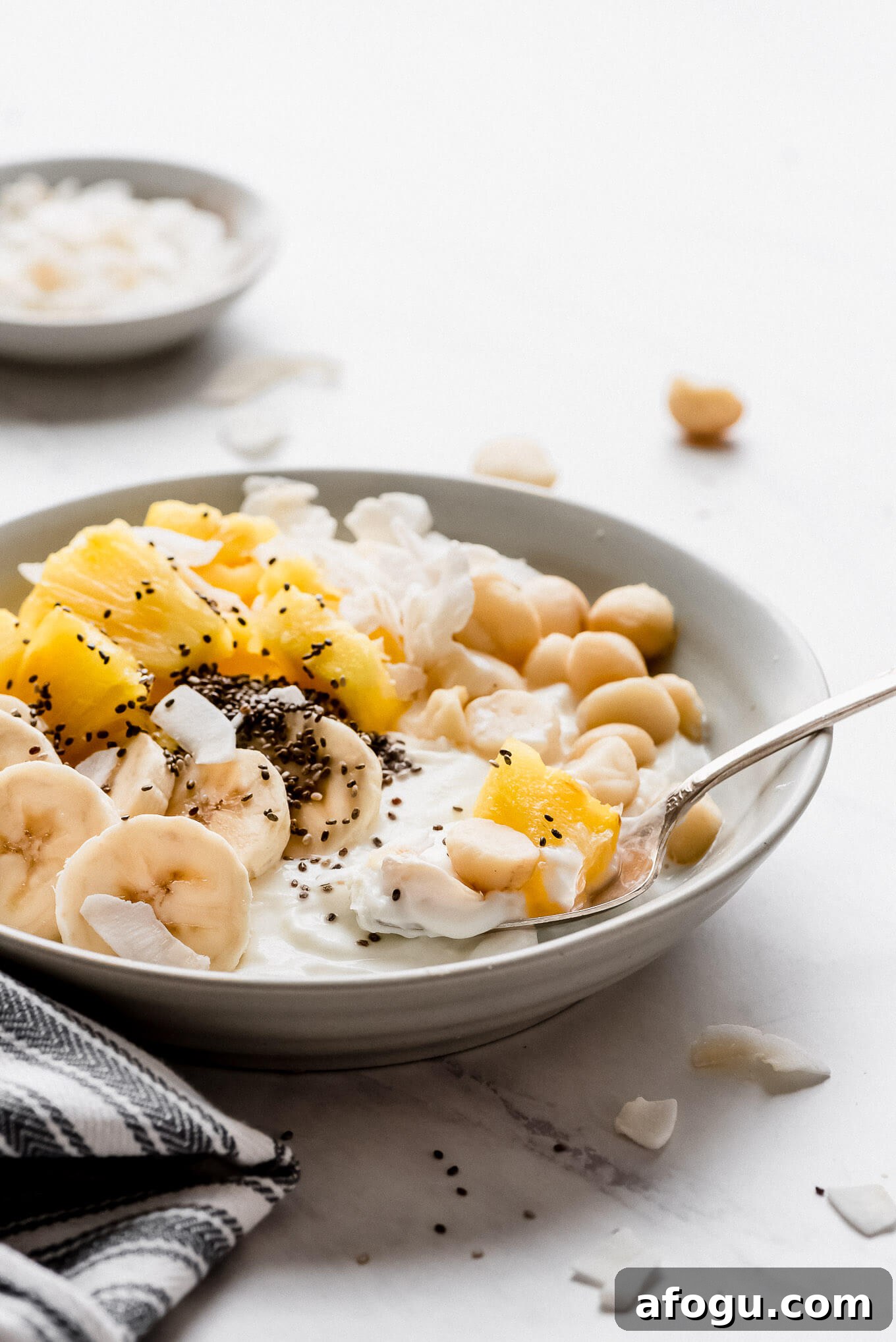 Tropical Greek yogurt bowl. A Greek yogurt bowl topped with bananas, pineapple, chia seeds, coconut flakes, and macadamia nuts.