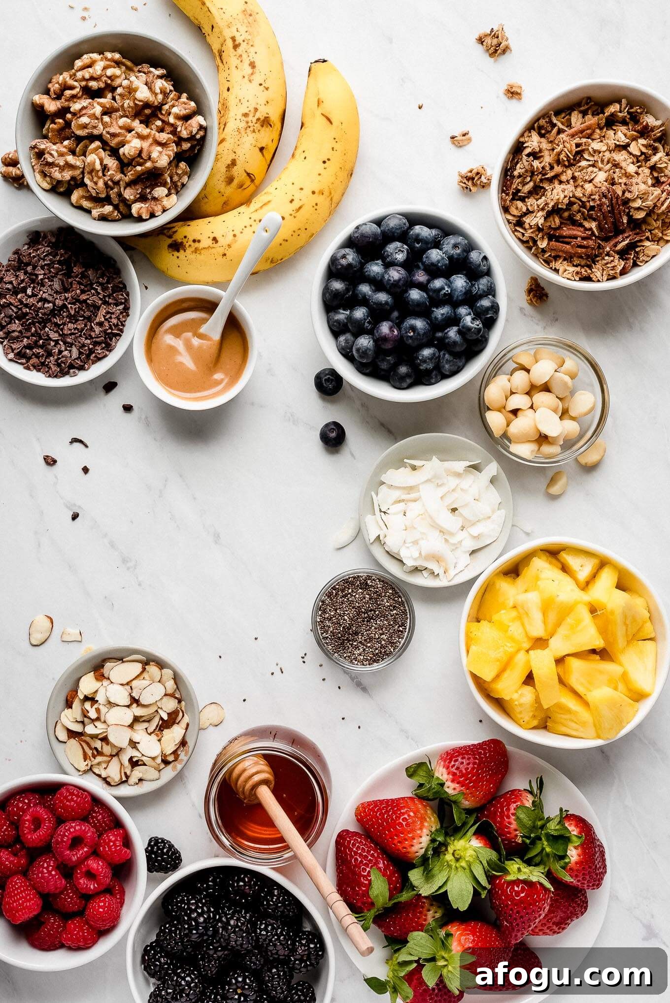 Ingredients for yogurt bowls. A bunch of bowls of various fruits, nuts, seeds, granola, peanut butter, and honey.