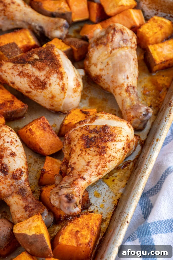 Close up of a chicken leg on a sheet pan surrounded by sweet potatoes.
