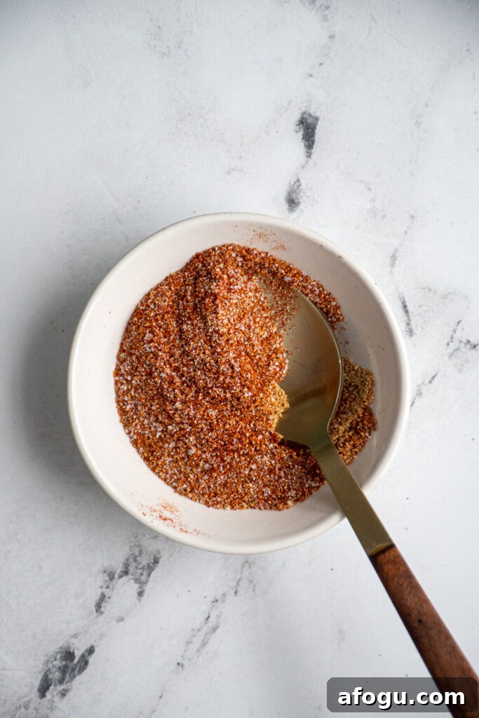 A small bowl with a spoon with the seasoning mixture for the chicken and sweet potatoes.