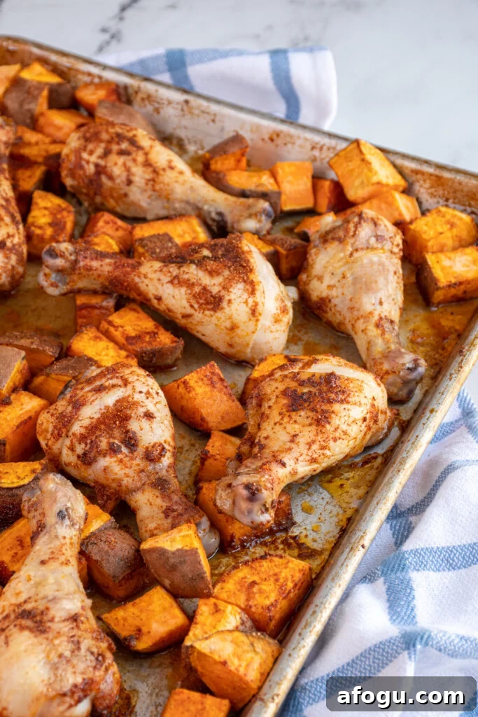 Photo of part of a sheet pan that is full of baked chicken legs and sweet potato chunks.