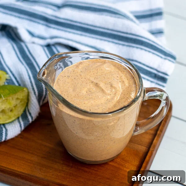 Serving glass with handle filled to the top with healthy southwest sauce sitting next to a kitchen towel and spoon.