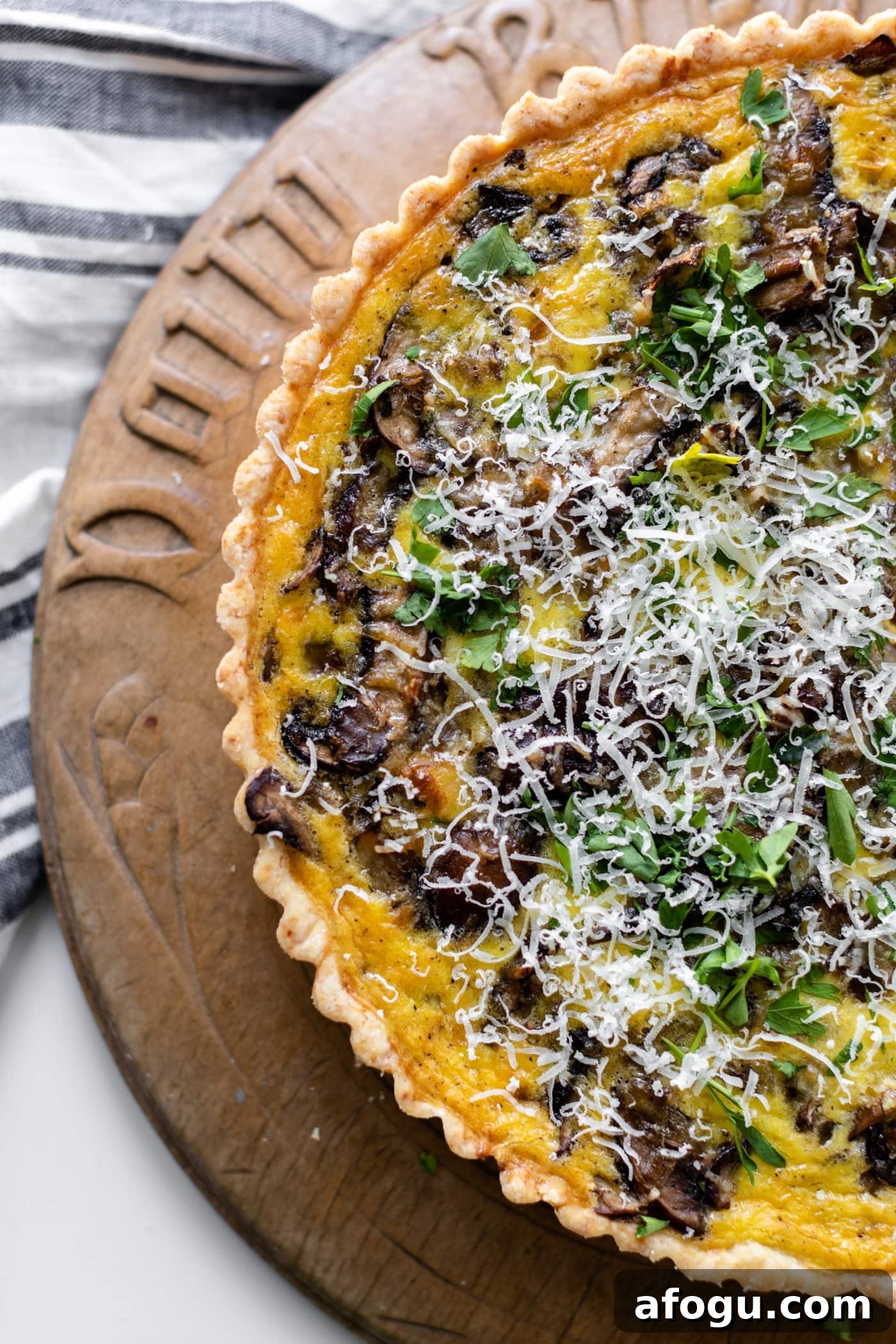 Breakfast quiche topped with parsley and Parmesan cheese sitting on bread board with linen underneath all on white surface