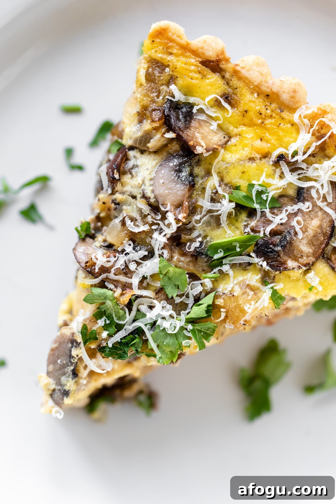 Piece of breakfast quiche topped with parsley and Parmesan cheese sitting on white plate