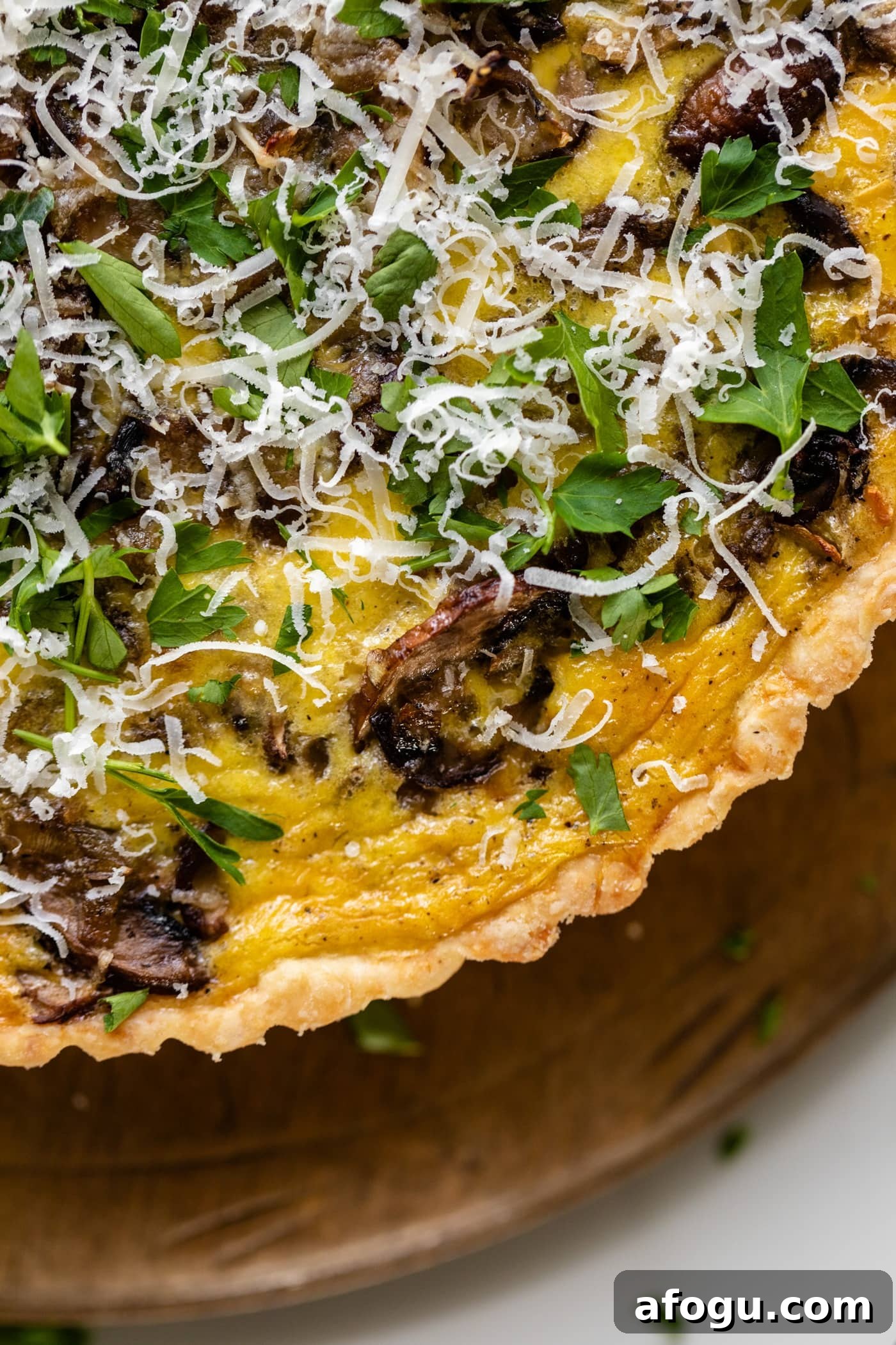 Breakfast quiche topped with parsley and Parmesan cheese sitting on bread board on white sufrace