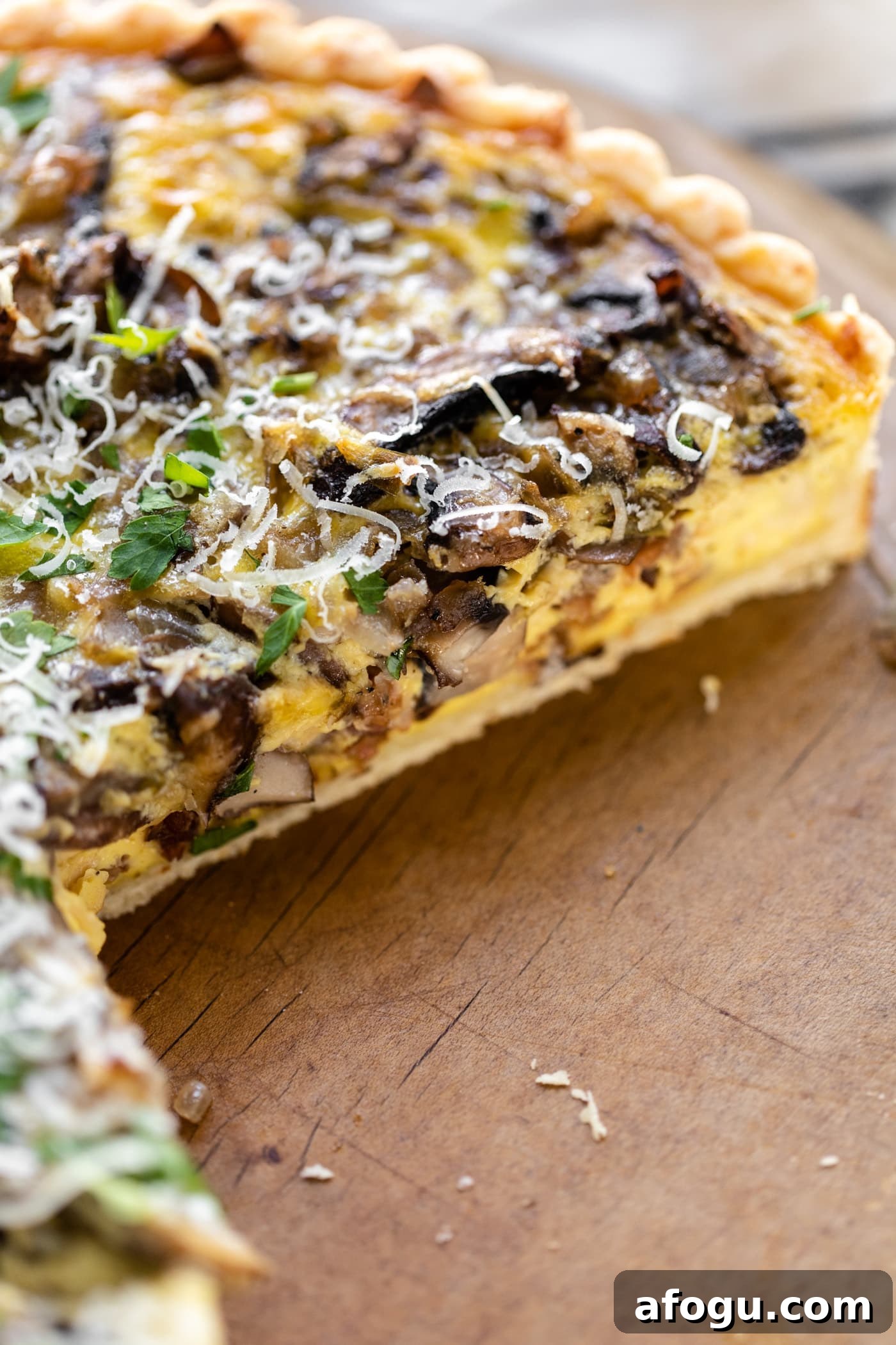 Breakfast quiche topped with parsley and Parmesan cheese sitting on bread board with pieces cut out revealing middle of quiche