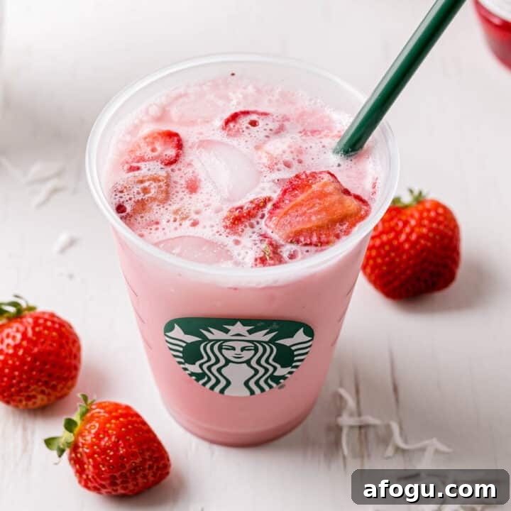Starbucks copycat pink drink in a Starbucks cup with a green straw next to fresh strawberries.