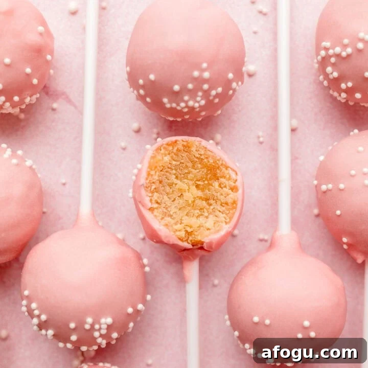 Several gluten-free pink cake pops lined up on pink surface, one with bite taken.