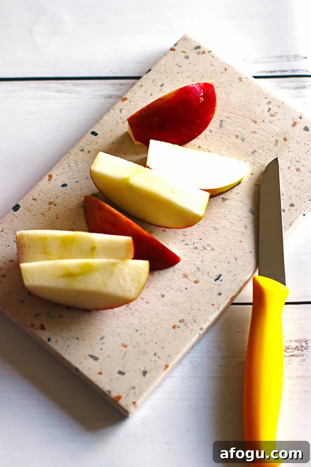 An apple sliced into medium pieces on a cutting board with a knife