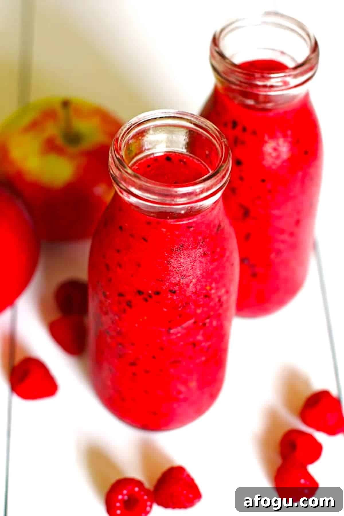 A red smoothie made of apples and berries that is sitting on a white table.
