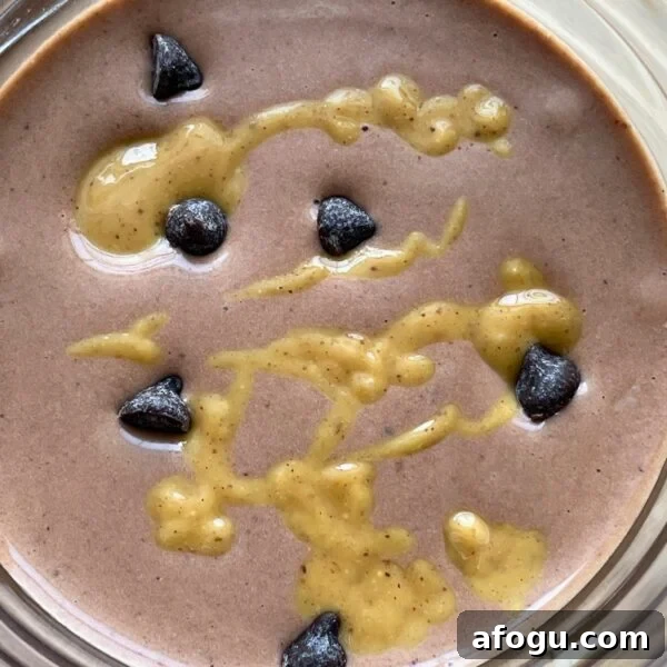 A chocolate peanut butter and banana smoothie with peanut butter drizzled over the top and chocolate chips sprinkled around.