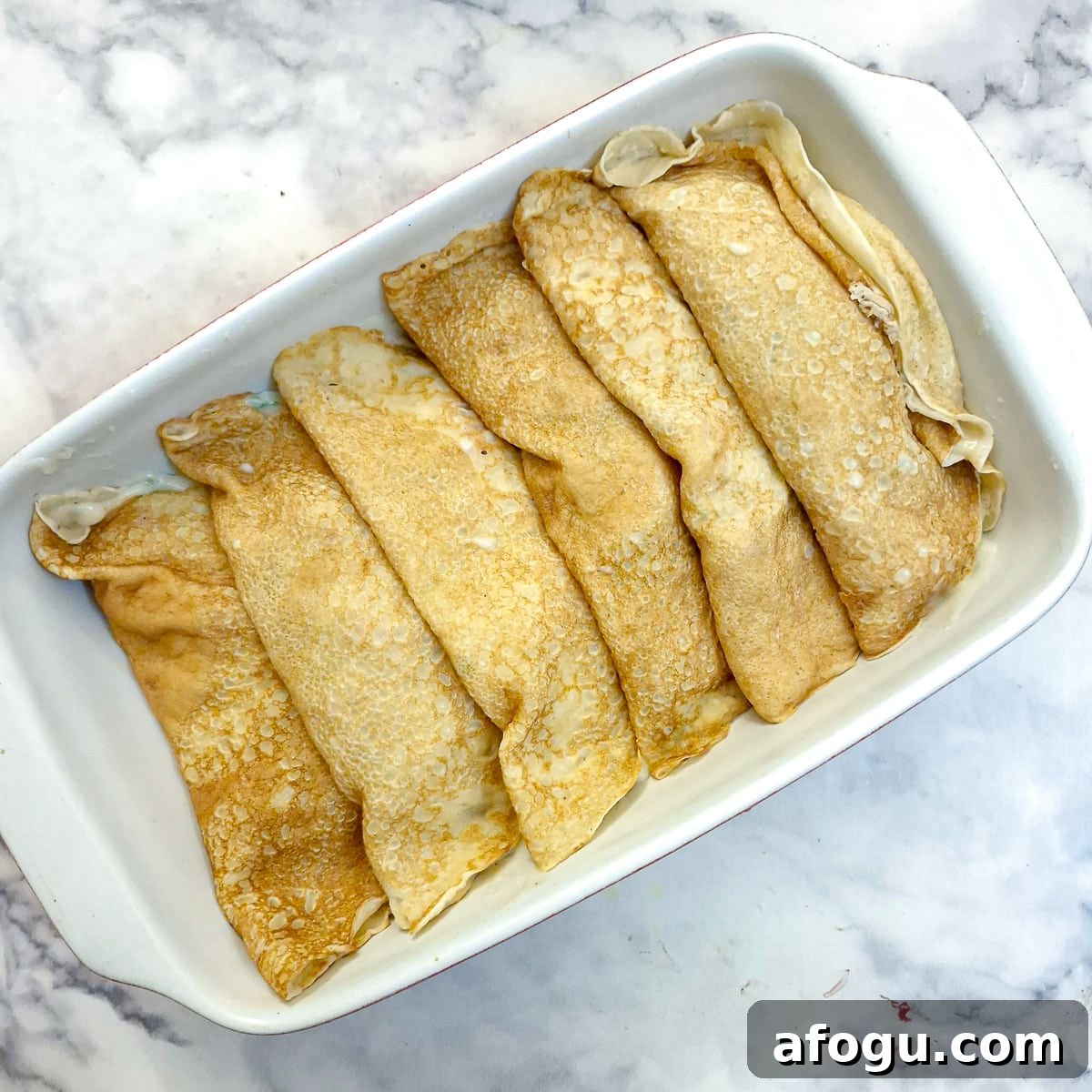 6 stuffed pancakes in a baking dish.