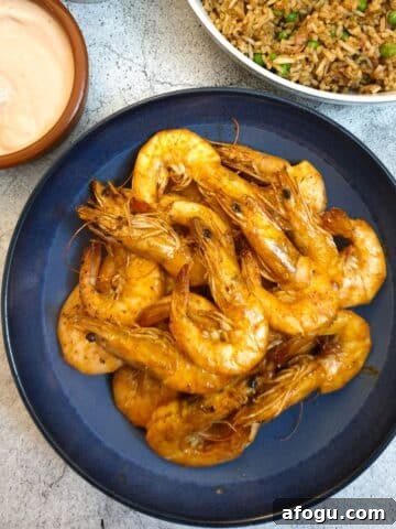 A dish of garlic butter prawns in their shells on a serving dish next to a bowl of fried rice and a pink dipping sauce.