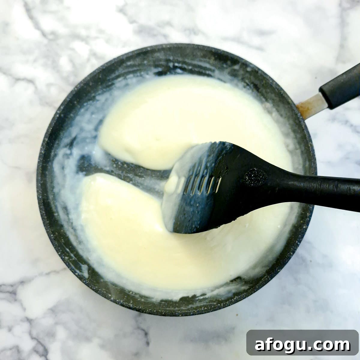 Cheese sauce in a frying pan with a spatula being pulled through to leave a trail.