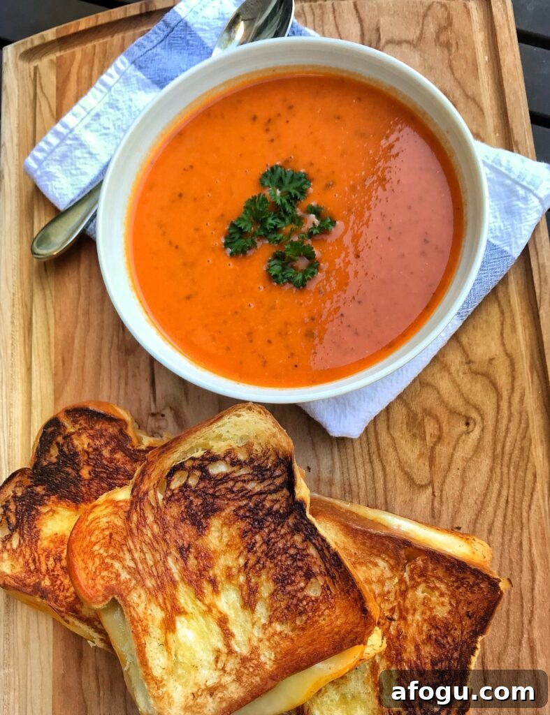 A bowl of tomato soup next to a stack of grilled cheese sandwiches