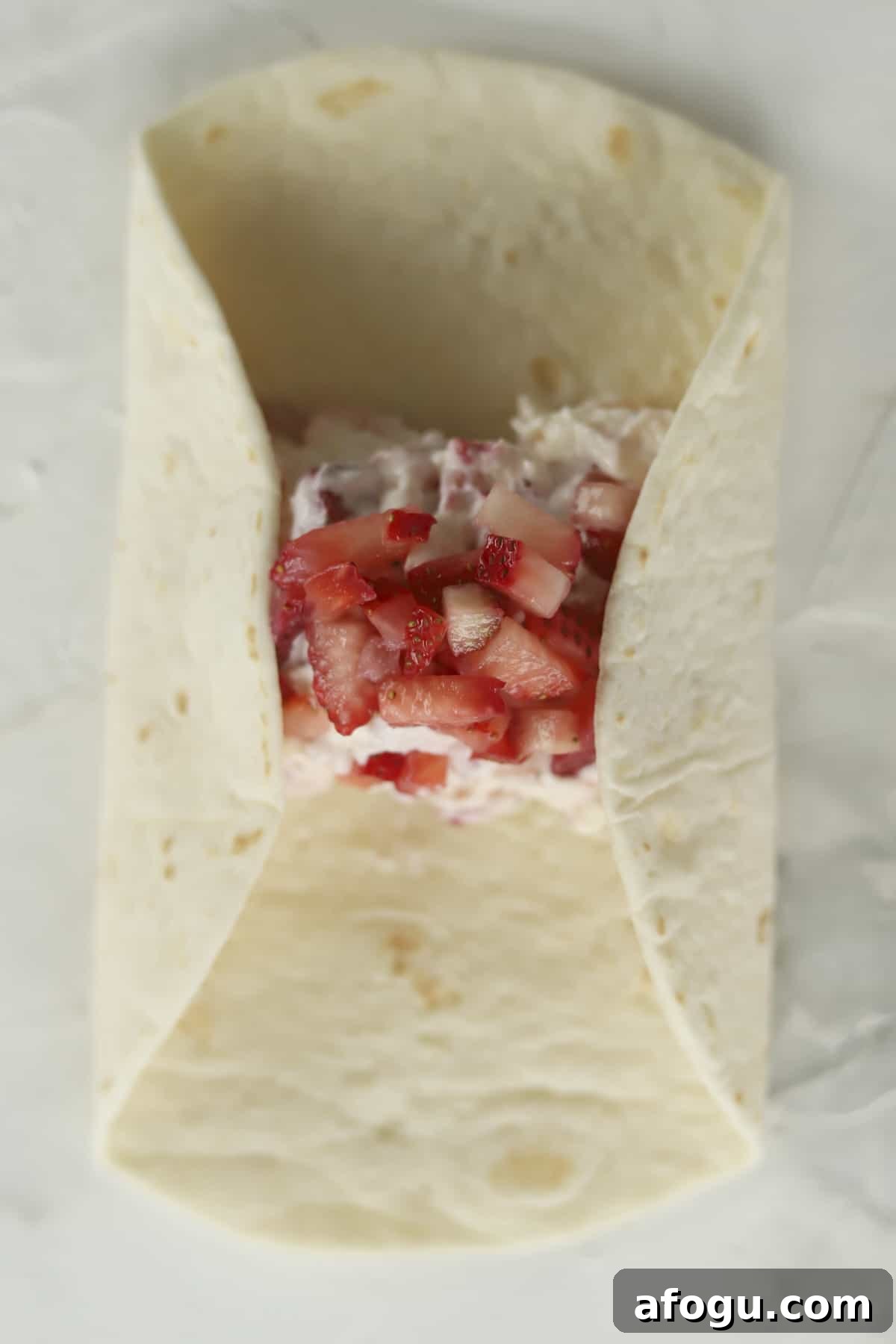 a tortilla being folded with a strawberry cheesecake filling