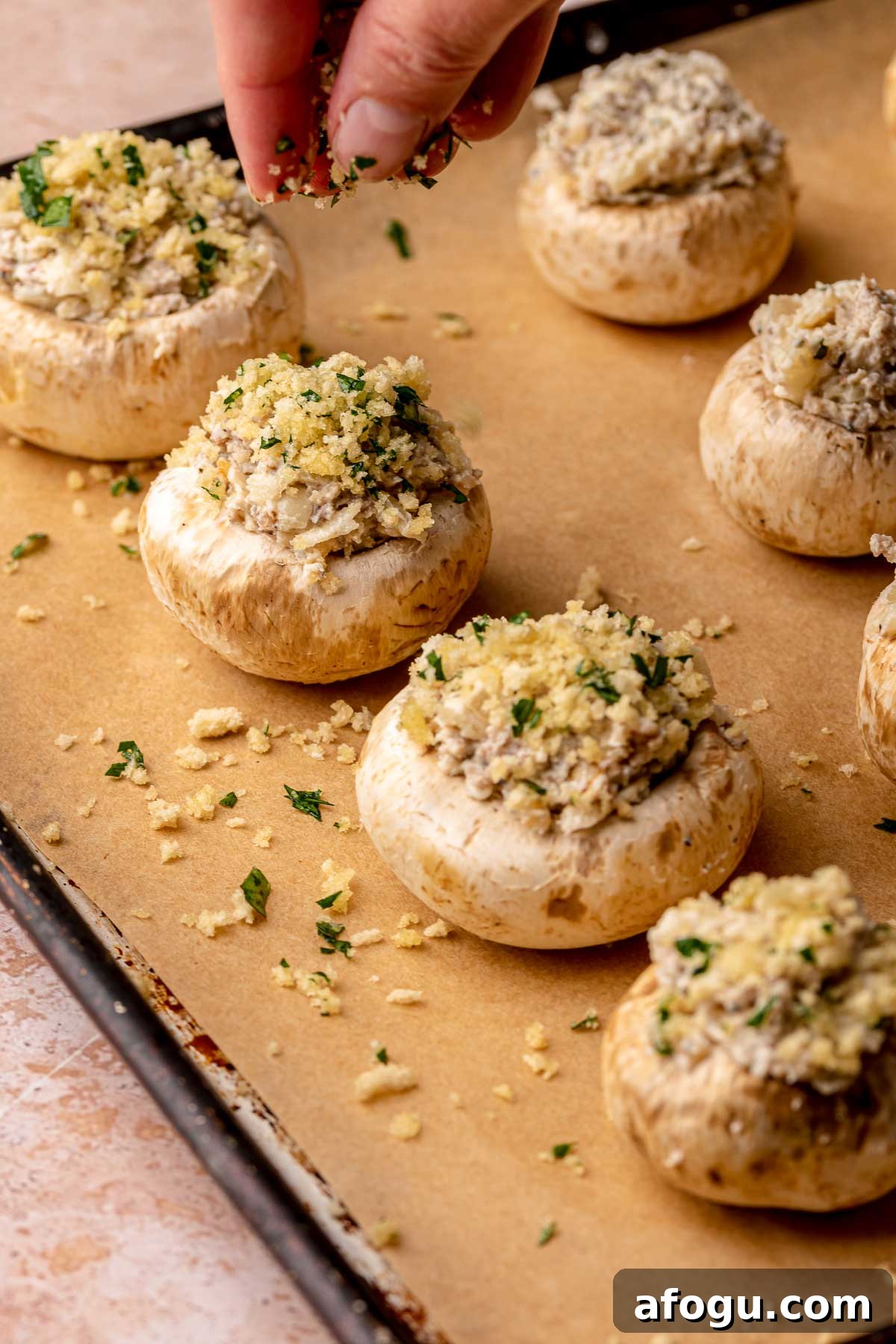 A hand sprinkles panko breadcrumbs on top of stuffed mushrooms.
