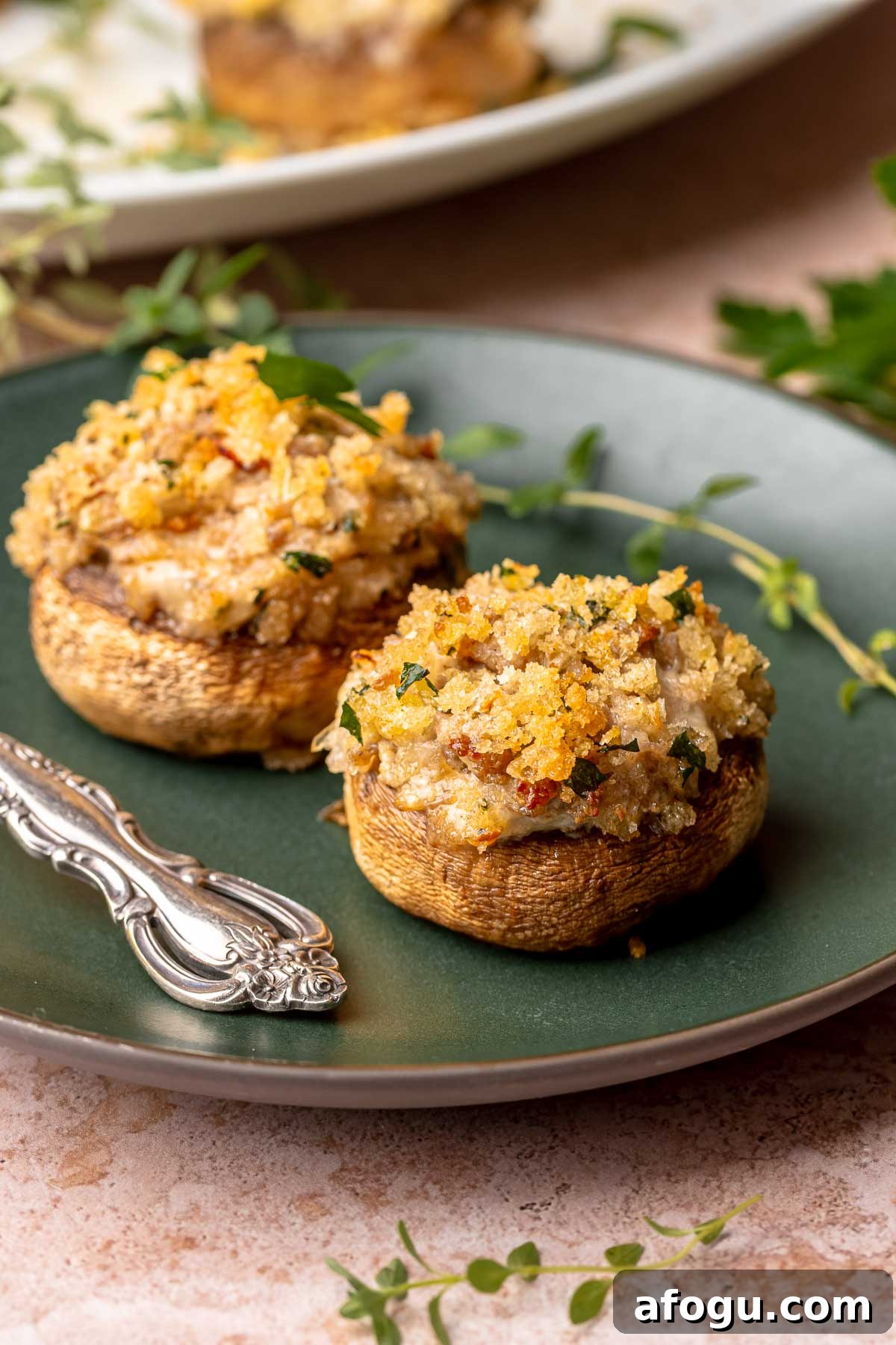 Two sausage and boursin stuffed mushrooms on a plate with a fork.