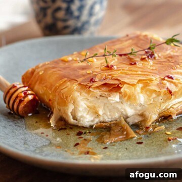 Phyllo fried feta cut open on a plate with a honey stick next to it.