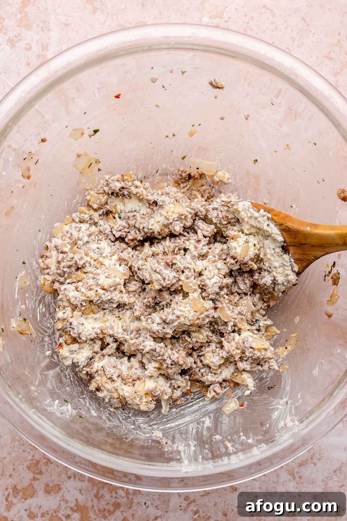 A wooden spoon mixes sausage and cheese filling in a bowl.