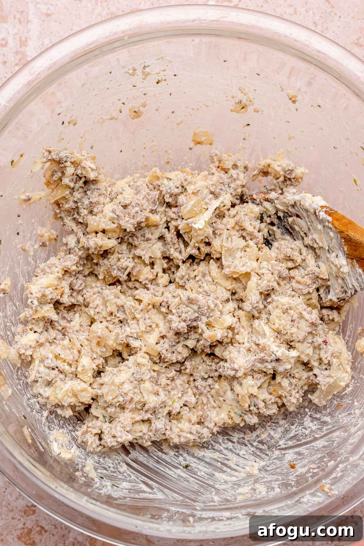 A wooden spoon mixes sausage and cheese filling in a bowl.