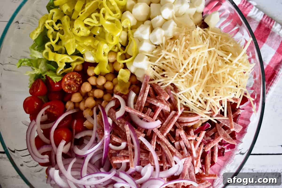 Lettuce, salami, red onion, cheese, pepperoncini, cherry tomatoes, and parmesan in a large glass bowl. 