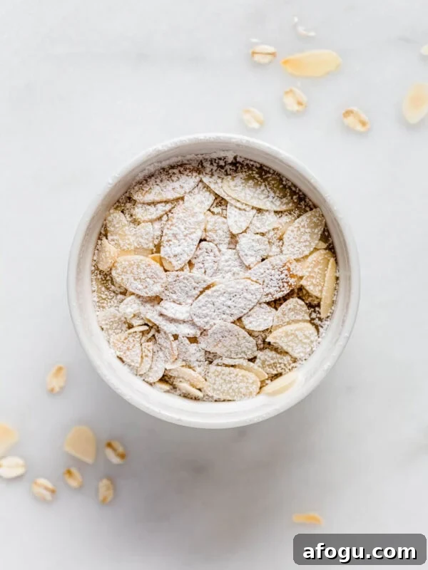 Almond croissant baked oats in a ramekin topped with sliced almonds and powdered sugar.