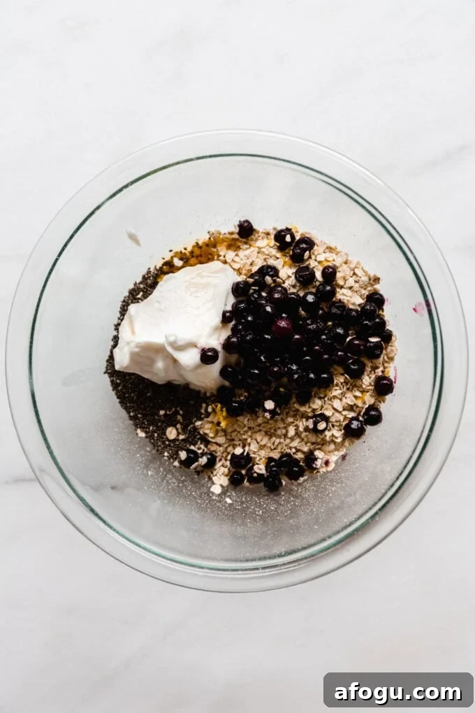 oats, yogurt, chia seeds and blueberries in a clear mixing bowl.