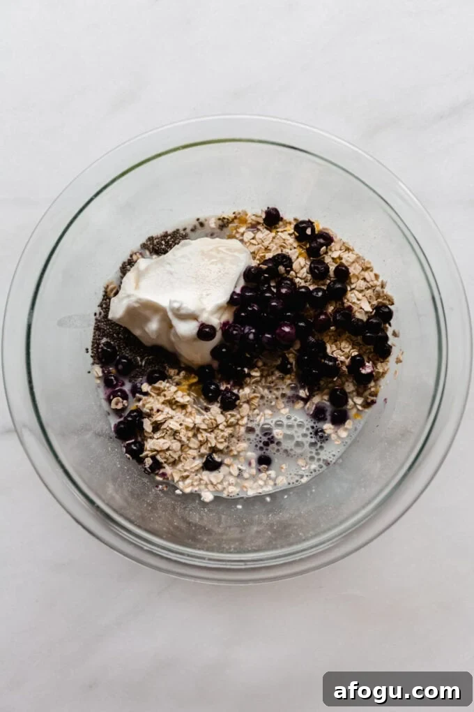 oats, chia seeds, yogurt, blueberries and almond milk in a clear mixing bowl.